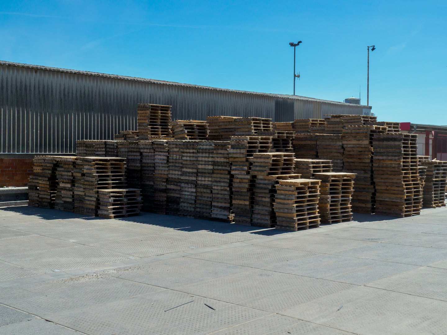Netjes gestapelde gebruikte houten pallets buiten een magazijn.